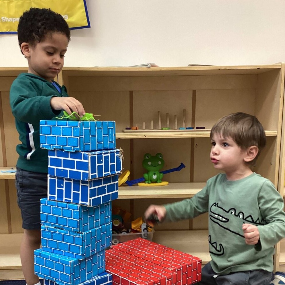 Two young children building a tall block tower in a preschool classroom
